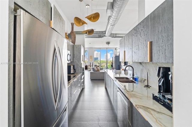 kitchen featuring modern cabinets, a sink, light stone counters, decorative light fixtures, and stainless steel appliances