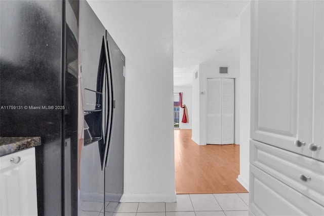 hallway with light tile patterned floors, visible vents, and a textured ceiling