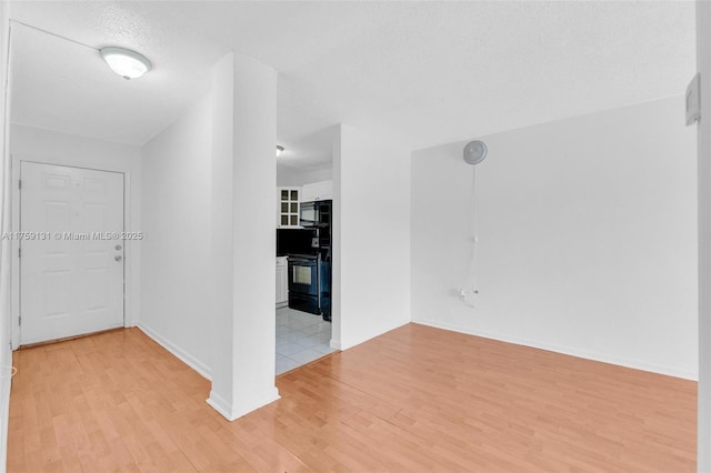 empty room featuring a textured ceiling, baseboards, and light wood-style floors