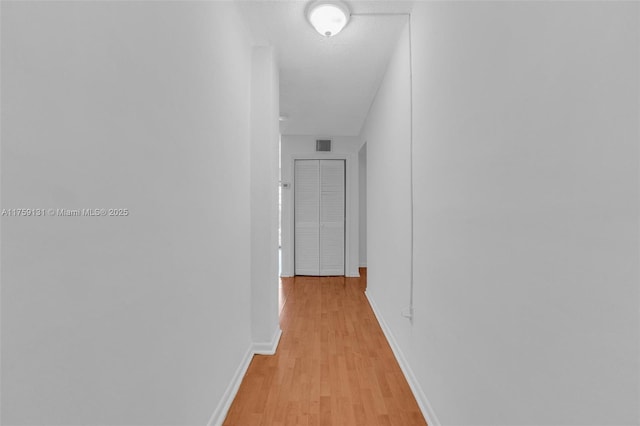 corridor with a textured ceiling, visible vents, light wood-type flooring, and baseboards