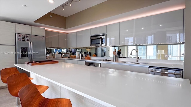 kitchen with gray cabinetry, a kitchen breakfast bar, appliances with stainless steel finishes, modern cabinets, and a sink