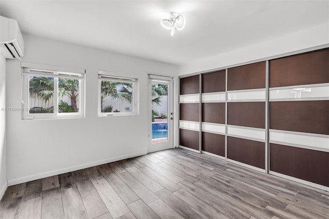 empty room with baseboards, an AC wall unit, and wood finished floors