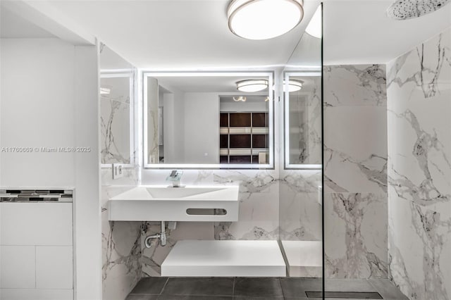 bathroom with a marble finish shower, tile walls, and a sink