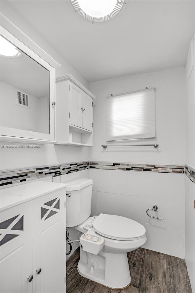 half bathroom featuring visible vents, toilet, tile walls, and wood finished floors