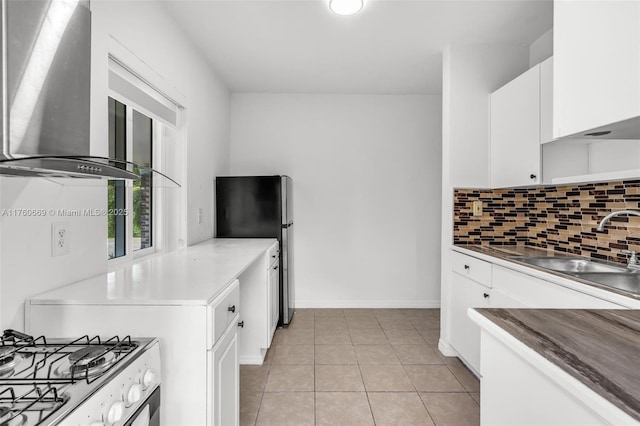 kitchen with backsplash, gas range oven, white cabinetry, wall chimney exhaust hood, and light tile patterned floors