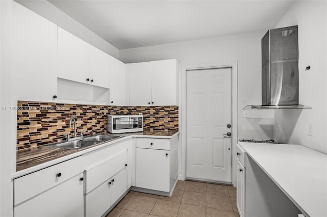 kitchen featuring a sink, stainless steel microwave, backsplash, white cabinetry, and light tile patterned floors