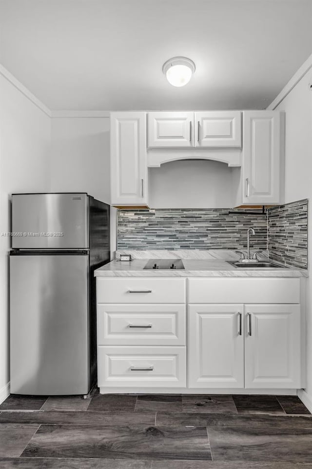 kitchen featuring decorative backsplash, white cabinetry, freestanding refrigerator, and a sink