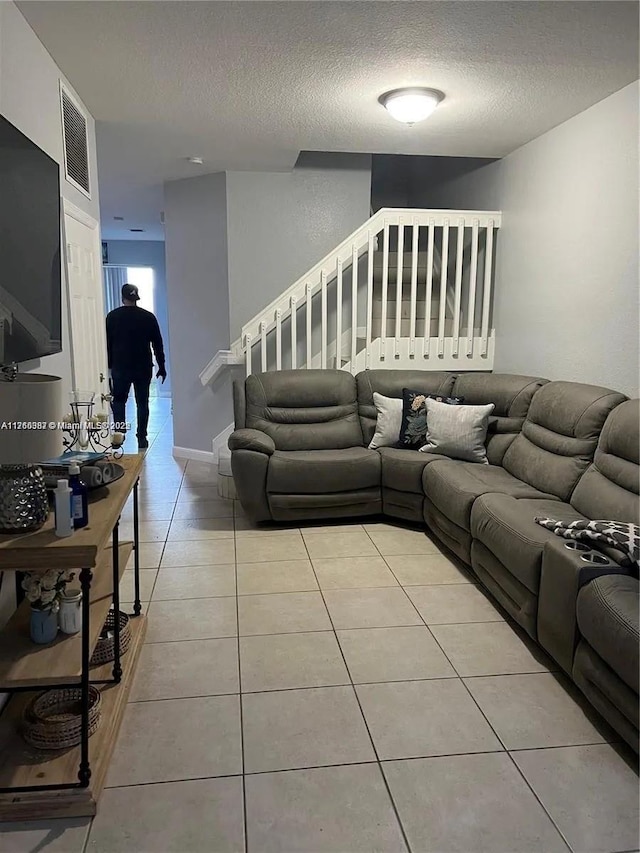 living area featuring stairway, light tile patterned flooring, visible vents, and a textured ceiling