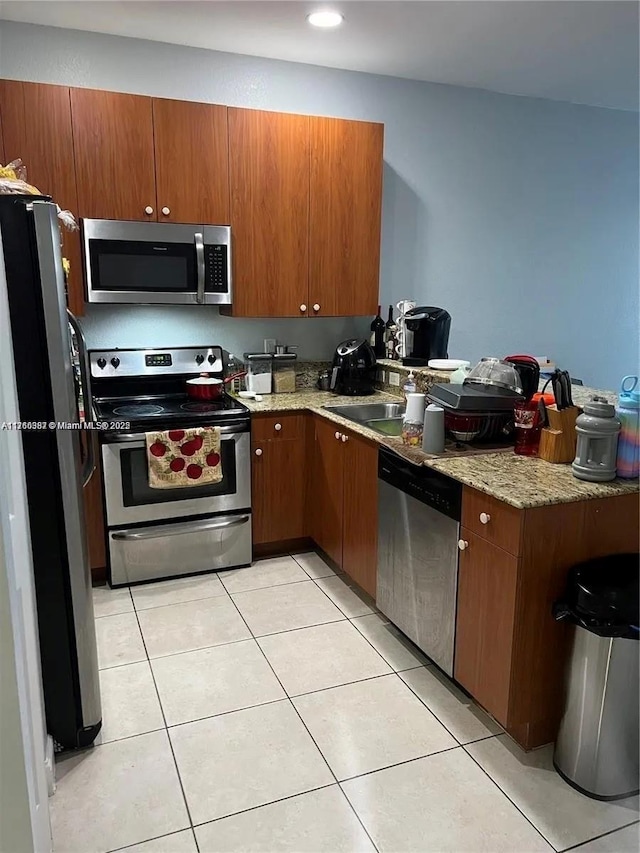 kitchen with light tile patterned floors, a peninsula, stainless steel appliances, and brown cabinetry