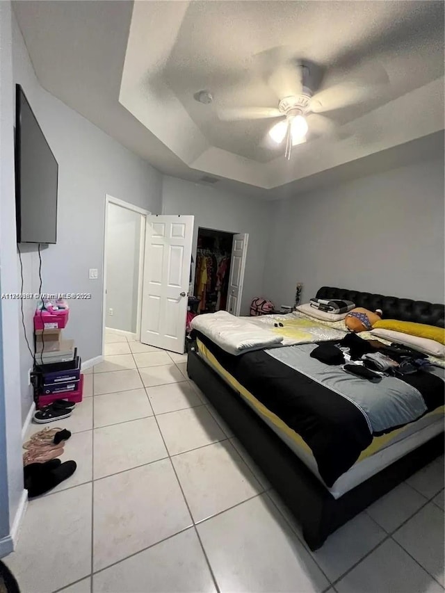 bedroom featuring a ceiling fan, a closet, baseboards, light tile patterned floors, and a raised ceiling