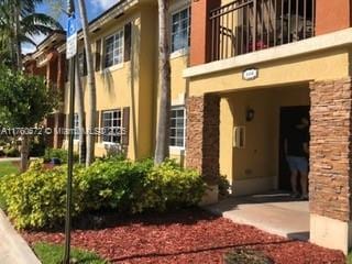 view of exterior entry featuring a balcony, stone siding, and stucco siding