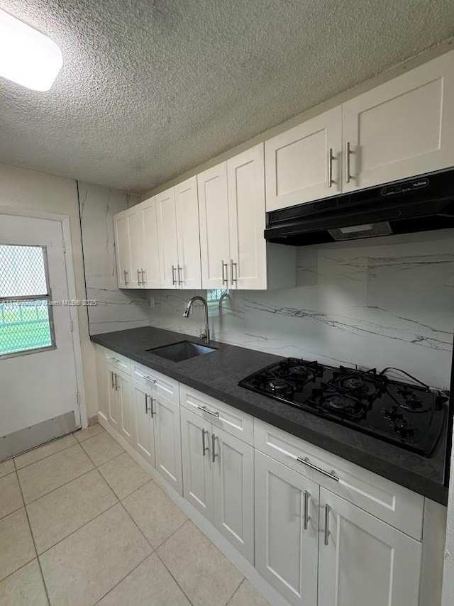 kitchen with a sink, under cabinet range hood, black gas cooktop, dark countertops, and white cabinetry