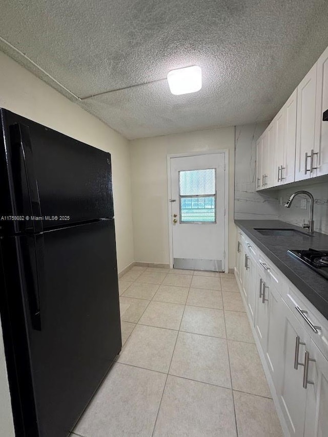 kitchen with dark countertops, black appliances, light tile patterned floors, white cabinetry, and a sink