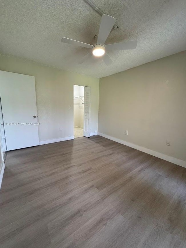 empty room with a textured ceiling, a ceiling fan, baseboards, and wood finished floors