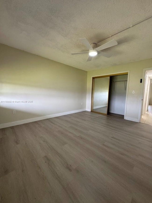 unfurnished bedroom with a closet, a textured ceiling, baseboards, and wood finished floors