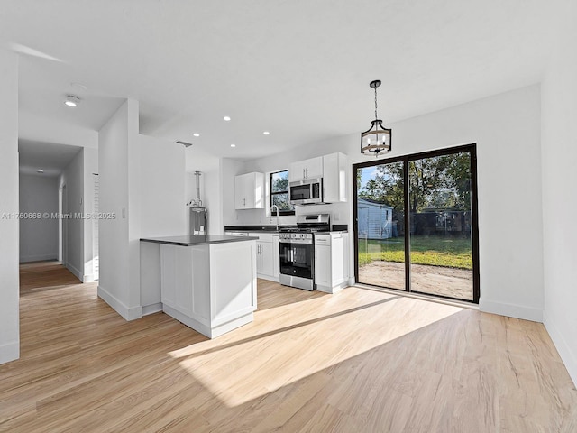 kitchen with light wood finished floors, a peninsula, stainless steel appliances, white cabinets, and dark countertops