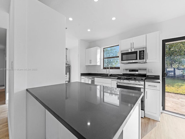 kitchen with recessed lighting, stainless steel appliances, white cabinets, light wood-style floors, and dark countertops