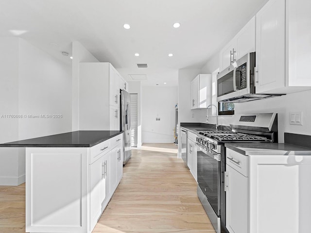 kitchen featuring light wood finished floors, a sink, stainless steel appliances, white cabinets, and dark countertops