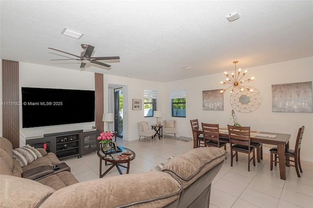 living area featuring visible vents, ceiling fan with notable chandelier, a textured ceiling, light tile patterned flooring, and baseboards