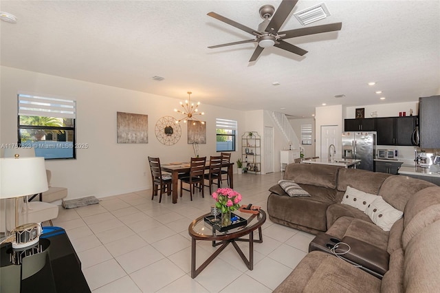 living area with light tile patterned flooring, ceiling fan with notable chandelier, a textured ceiling, and stairs