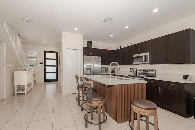 kitchen with light tile patterned floors, a sink, light countertops, appliances with stainless steel finishes, and a kitchen bar