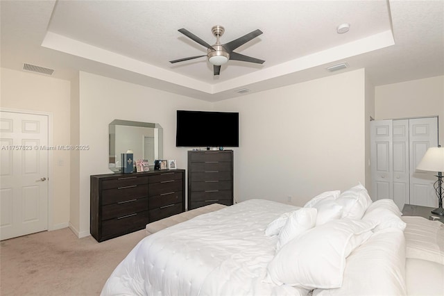 bedroom with a raised ceiling, light colored carpet, and visible vents