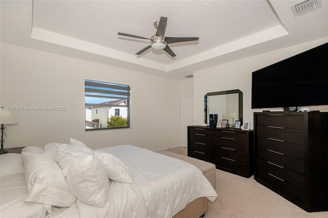 bedroom with a ceiling fan, a tray ceiling, light colored carpet, and visible vents