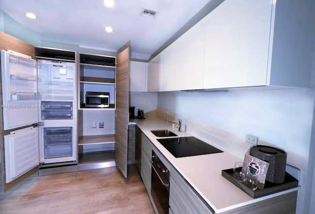 kitchen with visible vents, a sink, black appliances, white cabinets, and modern cabinets