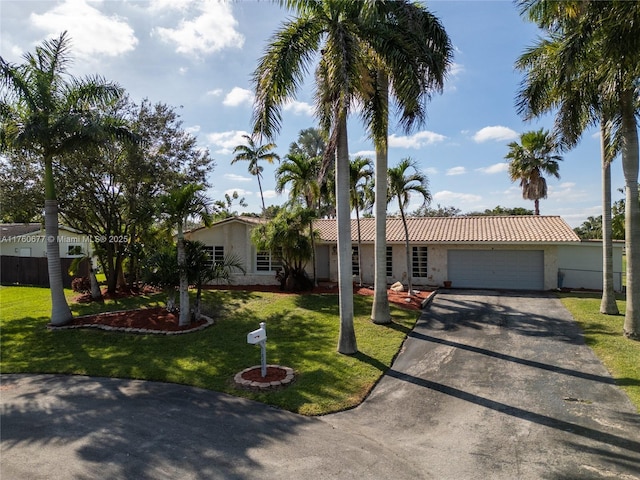 ranch-style home featuring aphalt driveway, stucco siding, an attached garage, and a front lawn