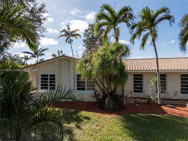 rear view of property with stucco siding, a yard, and a tile roof