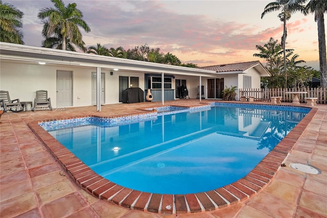 pool at dusk with a fenced in pool, fence, and a patio area