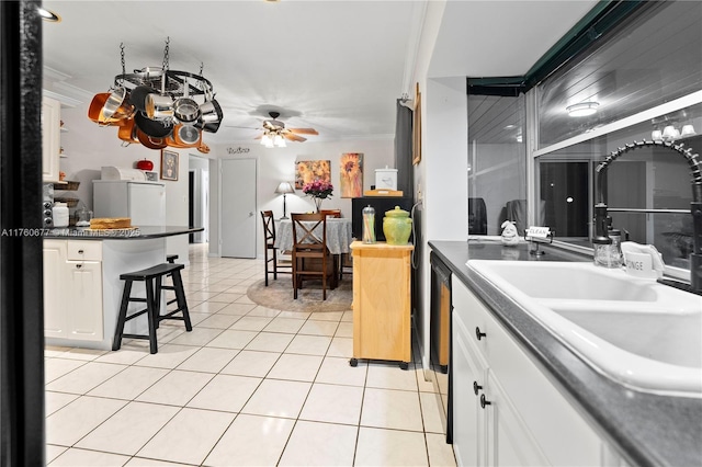 kitchen with light tile patterned flooring, white cabinets, a kitchen bar, and a sink