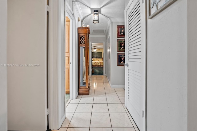 corridor with light tile patterned floors, baseboards, attic access, and ornamental molding