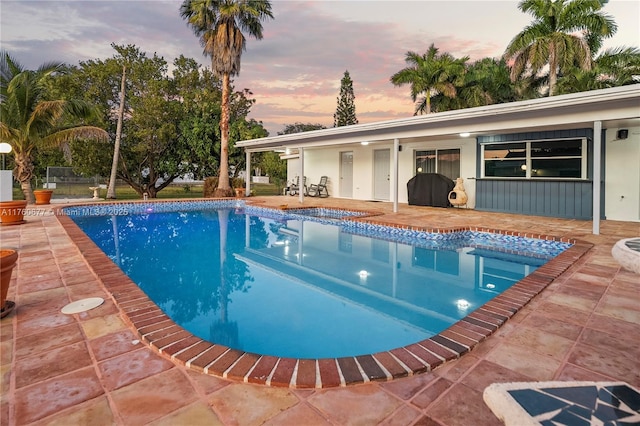 pool at dusk with a patio area and an outdoor pool