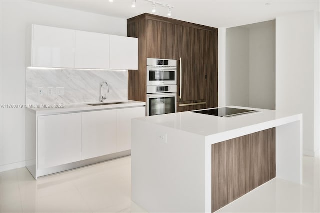 kitchen with backsplash, black electric stovetop, stainless steel double oven, modern cabinets, and a sink