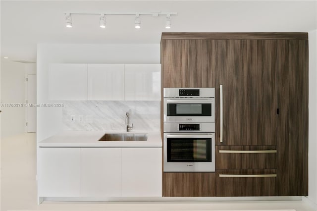 kitchen featuring modern cabinets, a sink, white cabinetry, stainless steel double oven, and light countertops