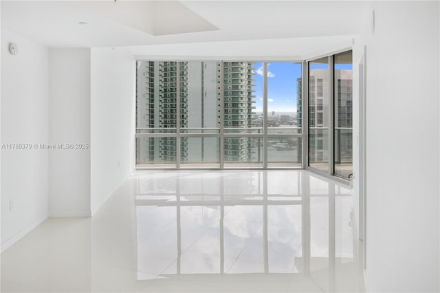 empty room with a city view, a wall of windows, baseboards, and tile patterned flooring