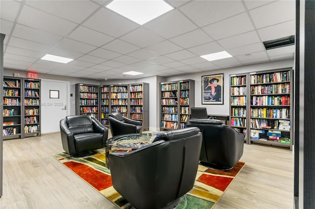 sitting room featuring bookshelves, wood finished floors, and a paneled ceiling