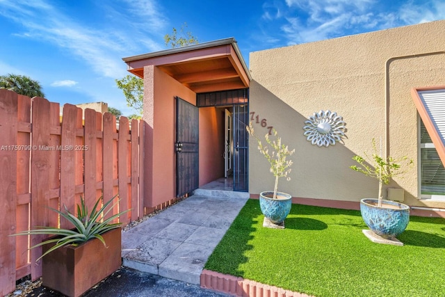 view of exterior entry featuring stucco siding, a yard, and fence