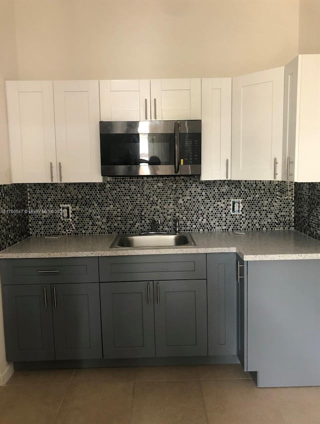 kitchen featuring gray cabinetry, a sink, stainless steel microwave, white cabinets, and decorative backsplash