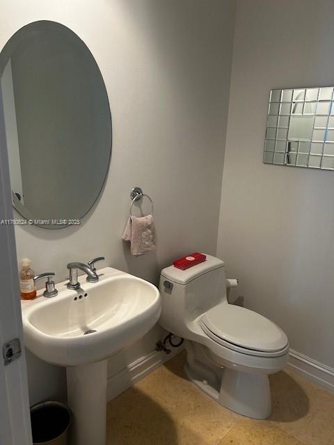 half bath with baseboards, toilet, and tile patterned flooring