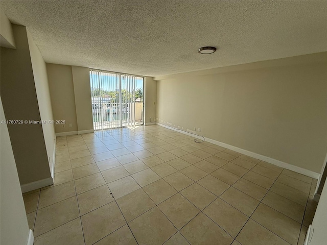 unfurnished room with a wall of windows, light tile patterned floors, baseboards, and a textured ceiling