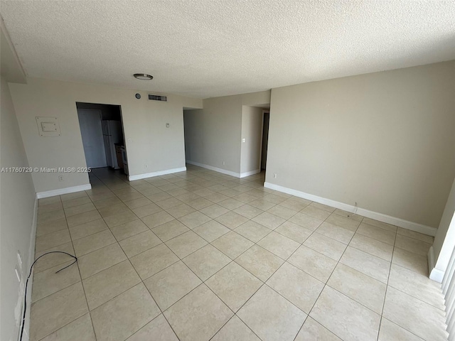 spare room with light tile patterned floors, visible vents, a textured ceiling, and baseboards