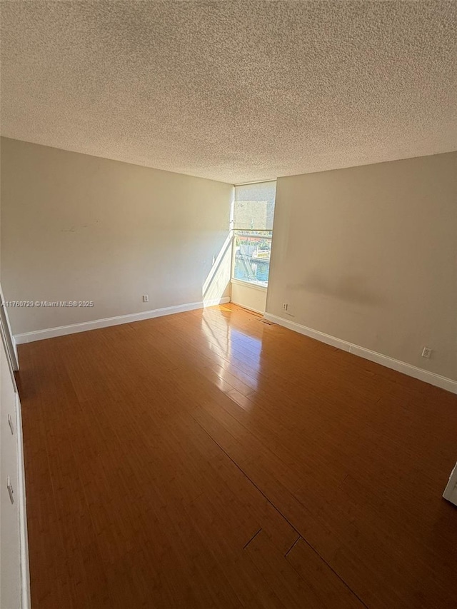 empty room with baseboards, a textured ceiling, and wood finished floors