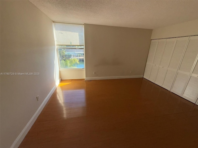 unfurnished bedroom with a closet, a textured ceiling, baseboards, and wood finished floors