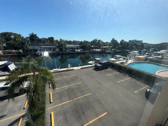 uncovered parking lot featuring an outdoor pool, a water view, and a boat dock