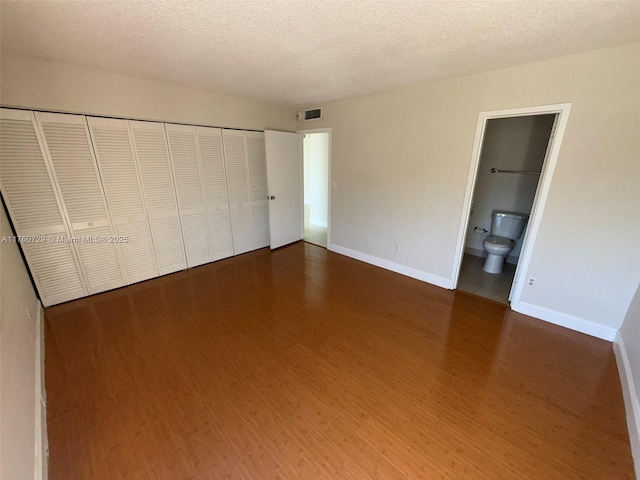 unfurnished bedroom with wood finished floors, visible vents, baseboards, a closet, and a textured ceiling