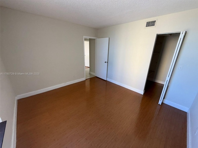 spare room with visible vents, baseboards, a textured ceiling, and dark wood-style flooring