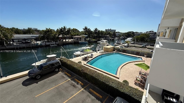 community pool with a water view, a boat dock, and a patio area