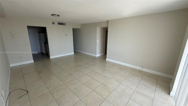 spare room with light tile patterned flooring, baseboards, visible vents, and a textured ceiling